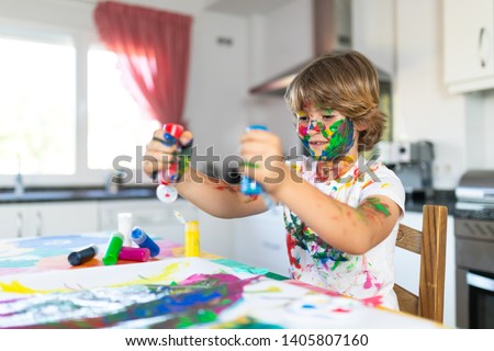 Cheerful child painting with colorful paint in the kitchen of his house
