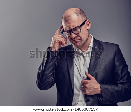 Thinking bald business man looking serious in eyeglasses having an idea and scratching the head in suit on grey background. Closeup studio portrait. 
