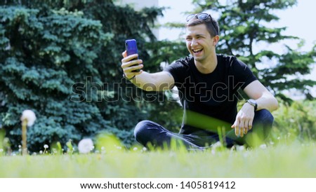 Happy man taking selfie on the smartphone. Spending time in the city park, sitting on the grass