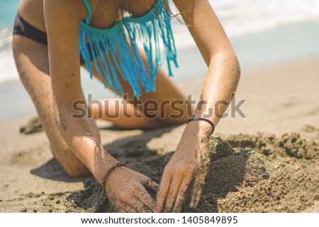 Young beautiful girl in bikini building a sand tower on the beach