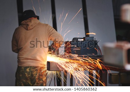 Industrial man working on cutting metal and steel with citcular saw with sharp blade. Focus on sparks. Sparks flowing over working table during metal grinding. Sparks while grinding iron
