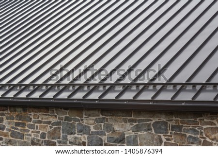 Standing seam modern metal roof over vintage stone wall, horizontal aspect Royalty-Free Stock Photo #1405876394