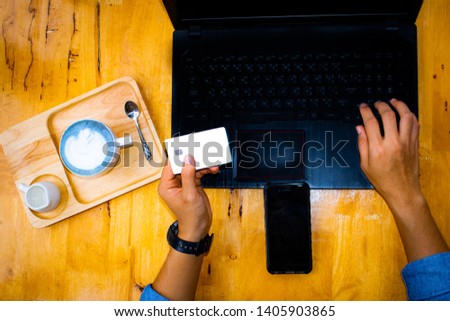 Close up, top view picture of female holding credit card while using laptop, banking and online shopping with blue coffee Latte art on the table.