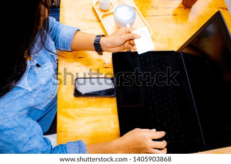 Close up, top view picture of female holding credit card while using laptop, banking and online shopping with blue coffee Latte art on the table.