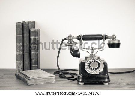 Vintage telephone, old books on table sepia photo