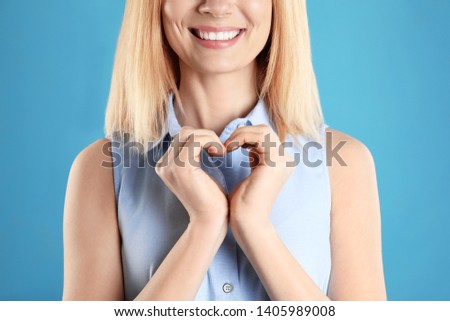 Woman making heart with her hands on color background, closeup