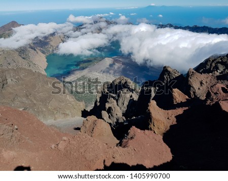 The barujari volcano surrounded by segara anak lake in the middle of the great caldera of Rinjani, a stunning morning view from the summit of Mount Rinjani with thin steaming clouds, Lombok. Indonesia
