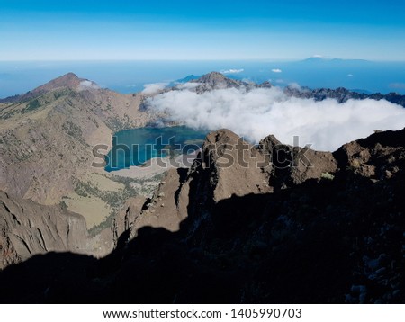 The barujari volcano surrounded by segara anak lake in the middle of the great caldera of Rinjani, a stunning morning view from the summit of Mount Rinjani with thin steaming clouds, Lombok. Indonesia