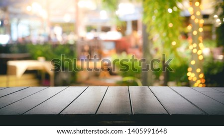 Empty wood table top and Blur light reflection green palm leaves or tree in tropical forest at restaurant, pub or bar at night. Blurred background for product display  with several concept.