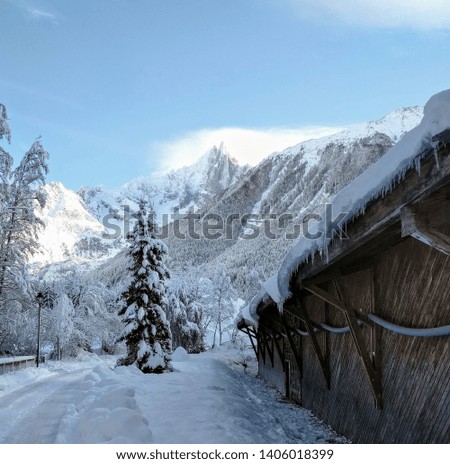 Snow and ice covered wooden building, and an alpine view. Chamonix valley, Haute-Savoie, France.