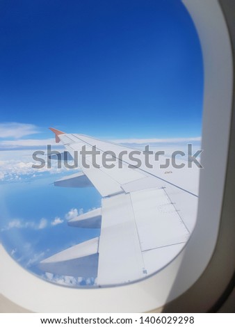 The wings of the plane on a cloud background and the bright sky. To shoot through a plane window