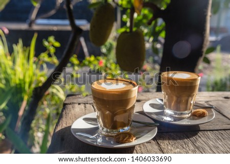 Two cups of latte with heart latte art on a wooden table greens and trees on the background. Bali, Indonesia. Concept of tropical holidays.