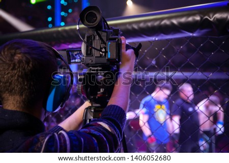 The operator shoots video at a sporting event. Professional video technician at work. Videographer for the event, rear view. The operator while working with a large professional camera.