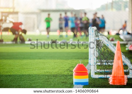 Marker cones and mini goal on green artificial turf for soccer training. Soccer equipment with blurry soccer team training in soccer academy.