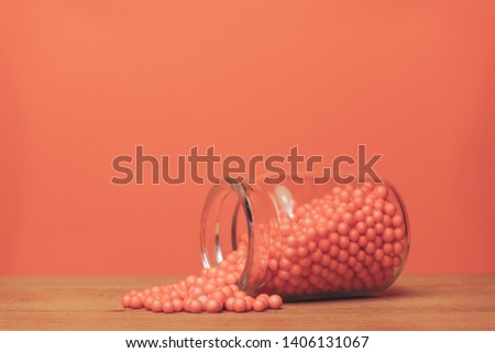 Small bottle of coral orange preparations (vitamins, dyes, flavor enhancers, nutritional supplements, innovative technologies, candy sweets) Blue wooden table and coral orange background. 