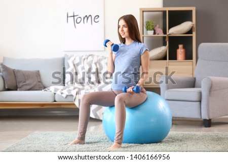 Beautiful pregnant woman with dumbbells and fitball training at home