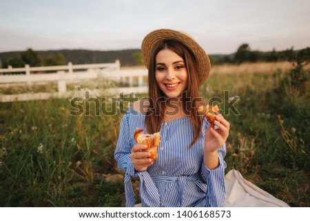 Pregnant woman in the field eating fresh backed crispy croissant. Healthy food. Young woman eats very appetizing. Background of farm