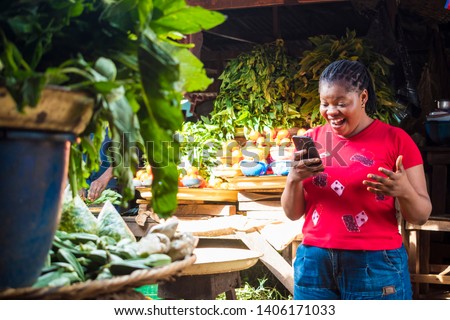 african lady in a local market surprised and excited by something she's viewing on a phone Royalty-Free Stock Photo #1406171033