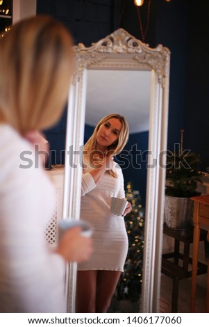 young girl in a woolen white dress looks at herself in the mirror