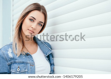 Beautiful young teenage girl blonde-haired female student  with denim jacket  posing outdoors, White background space for text