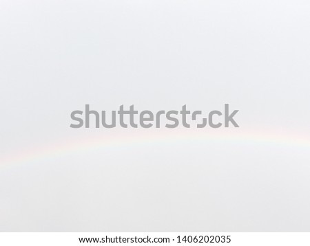 Blurry rainbow on greyish white sky for natural background. Rainbow path across the sky