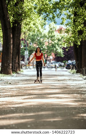 Skating woman on inline skate listening music on blue headphones in urban environment in spring with lots of white cotton seeds from the trees