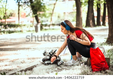 Beautiful girl is preparing for rollerblading at the road in the park