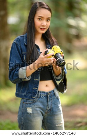 Portrait of beautiful young Asian woman with camera at summer green park 