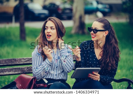 Two beautiful women holding a tablet pointing away in the street - Image