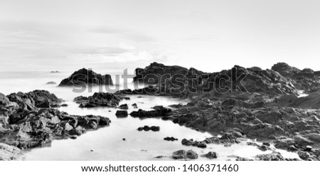 panoramic shot . long exposure rocky beach in high key,  black and white. 