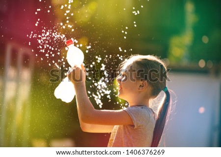splashes and drops of water in the sunlight. girl watering splashes of water from a bottle without a brand. cheerful girl playing with spray and water jets.