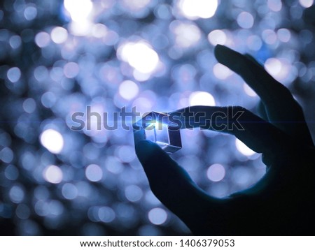 Silhouette of a male hand holding a glass cube with blue technology lighting illuminated effected and bokeh background. Selected focus.