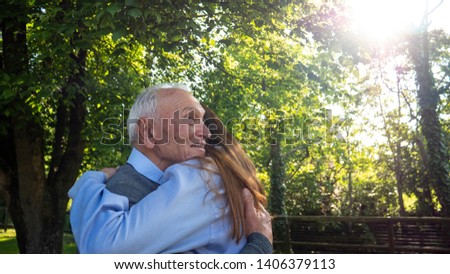 Portrait of happy granddaughter is giving an effective hug to her grandfather as a sign of love and respect in a green park on a sunny day.
