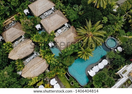 Aerial view of luxury hotel with straw roof villas and pools in tropical jungle and palm trees. Luxurious villa, pavilion in forest, Ubud, Bali Royalty-Free Stock Photo #1406404814