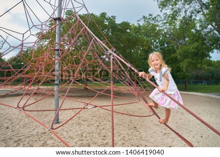 little girl smiling looking at camera, little child playing on climbing net . outdoors on sunny summer day.