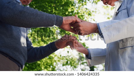 Close up of an young woman social worker or nurse is holding hands of senior patient as sign of care and support in a green park on a sunny day.