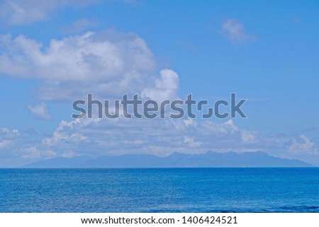Scene of deep blue sea and bright blue sky seeing mountains far behind.