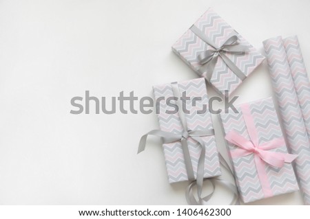 Process of wrapping gifts on white background. Gifts boxes in wrapping paper with white, pink and grey ribbons. Happy holidays concept. Top view. Flat lay