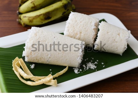  Puttu or white Pittu, top view of popular South Indian steamed breakfast dish made of rice flour,  grated coconut in bamboo mould with banana and Pappad Kerala, India. Sri lankan food on banana leaf.