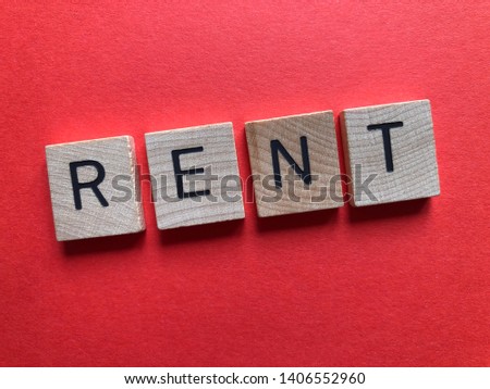 The word Rent in wooden alphabet letters on a plain red background with copy space. Creative concept, banking and finance
