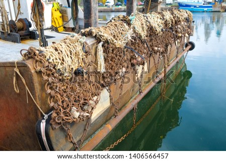 The rear side of a fishing boat in the harbor, showing the nets and chains