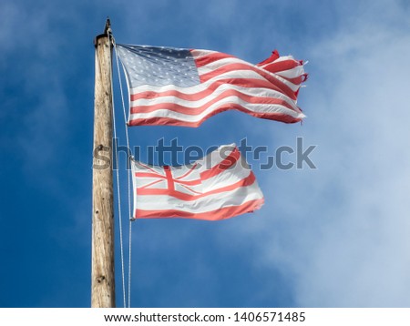 Faded and worn Hawaiian and American flags on a wooden flagpole 