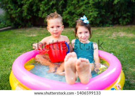 Subject childhood summer games in the yard. Caucasian brother and sister playing plastic toys bucket sitting in the water, inflatable round children's pool. Summer is hot, rest in swimsuits.