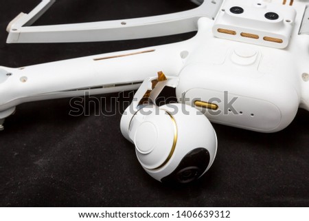 Broken white drone after a fall. Isolated on a black background. Damaged body and stabilizer camera gimbal. Plugged cable loop Close up. Device to repair