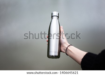 Close-up of steel eco thermo water bottle in female hand. Royalty-Free Stock Photo #1406645621