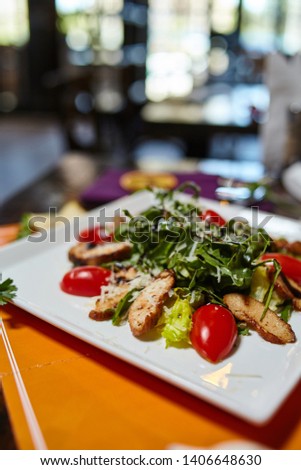 Dietary meat salad clseup photo - fried meat slices with greenery, vegetables and cheese on a white plate. Blurry background