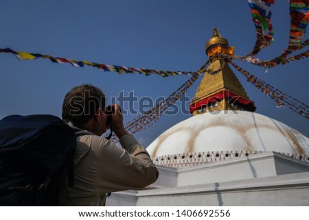unkhown tourist with backpack holding camera and taking photo at the famous Boudhanath pagoda and prayer flags in Kathmandu the capital city of Napal