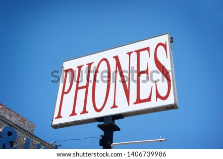 Aged and worn urban phones sign with blue sky                              