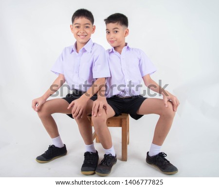 Little Asian sibling boys in student uniform pose together on white background