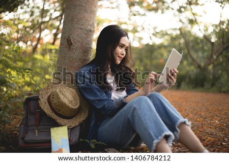 
Women sit under the tree and use The tablet has pockets and maps, evening light, travel ideas.